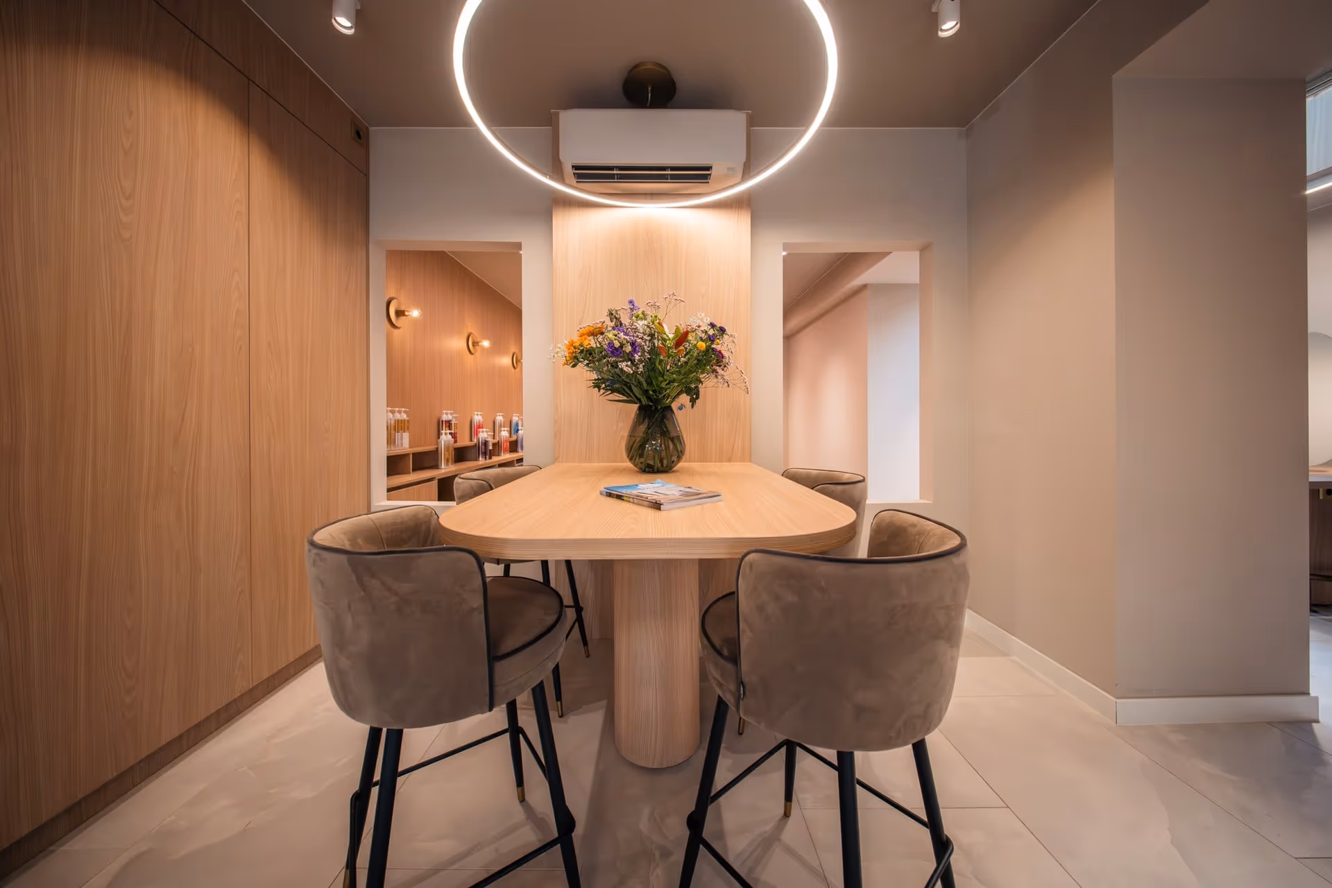 Moderne eethoek met een houten tafel, vier gestoffeerde stoelen, een vaas met kleurrijke bloemen en een ronde plafondlamp.