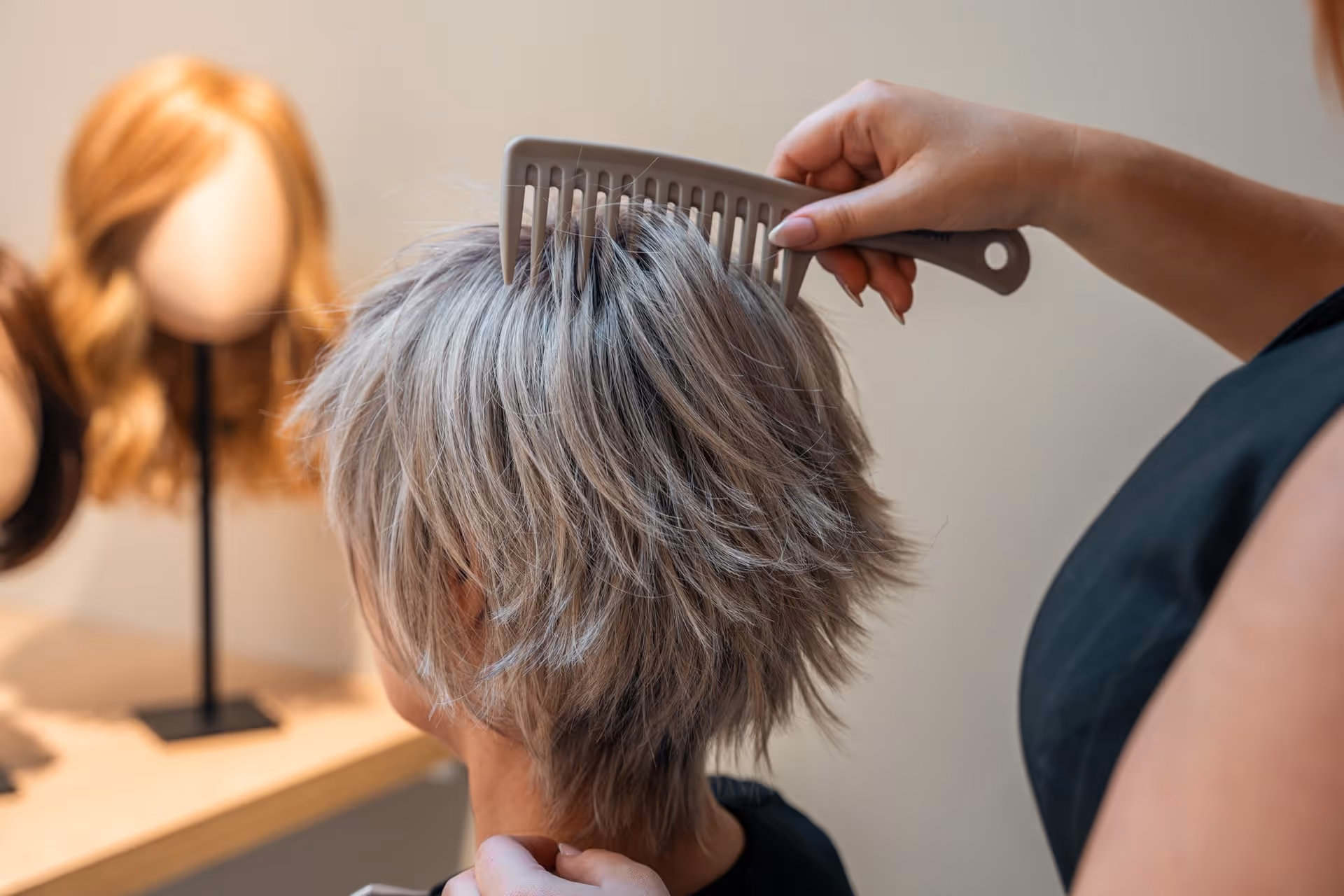 Persoon die kort, gelaagd grijs haarwerk kamt in een kapsalon met mannequinhoofden op de achtergrond.