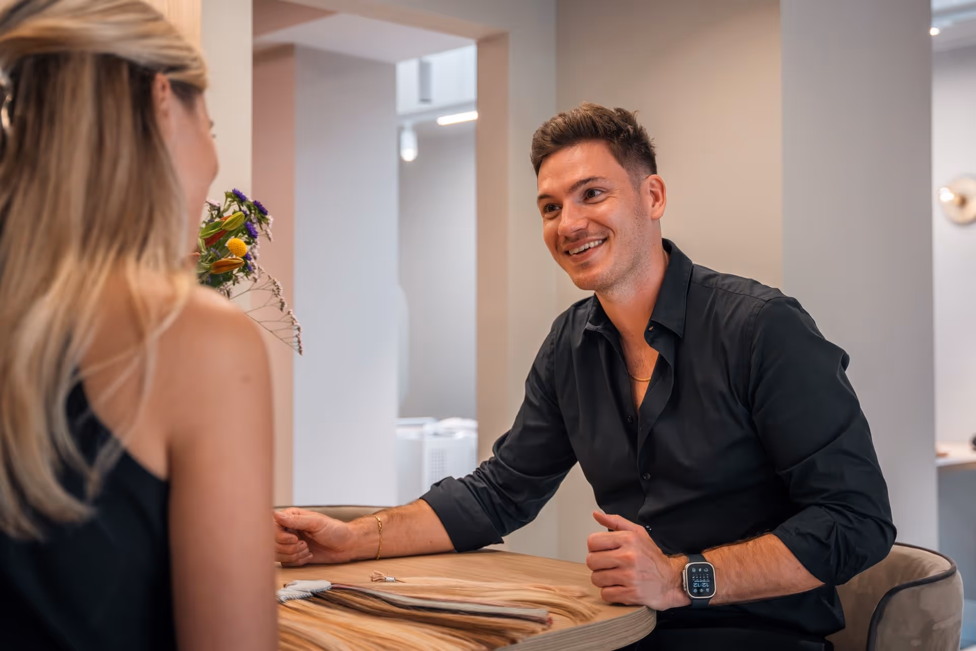 Skelte draagt een zwarte blouse; glimlacht en spreekt tegen een blonde vrouw; met haar extensies samples.