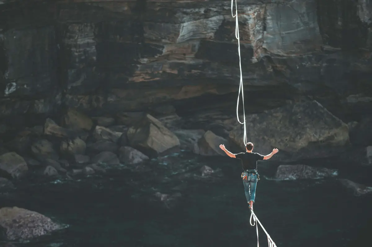 homme sur une corde entre deux falaises illustrant le danger
