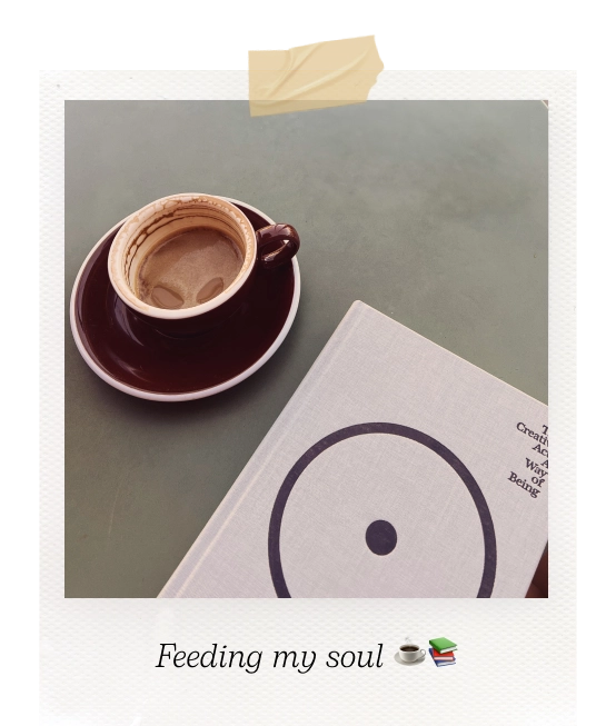 Polaroid picture of a cappuccino cup and a book on a table. Caption reads "Feeding my soul".