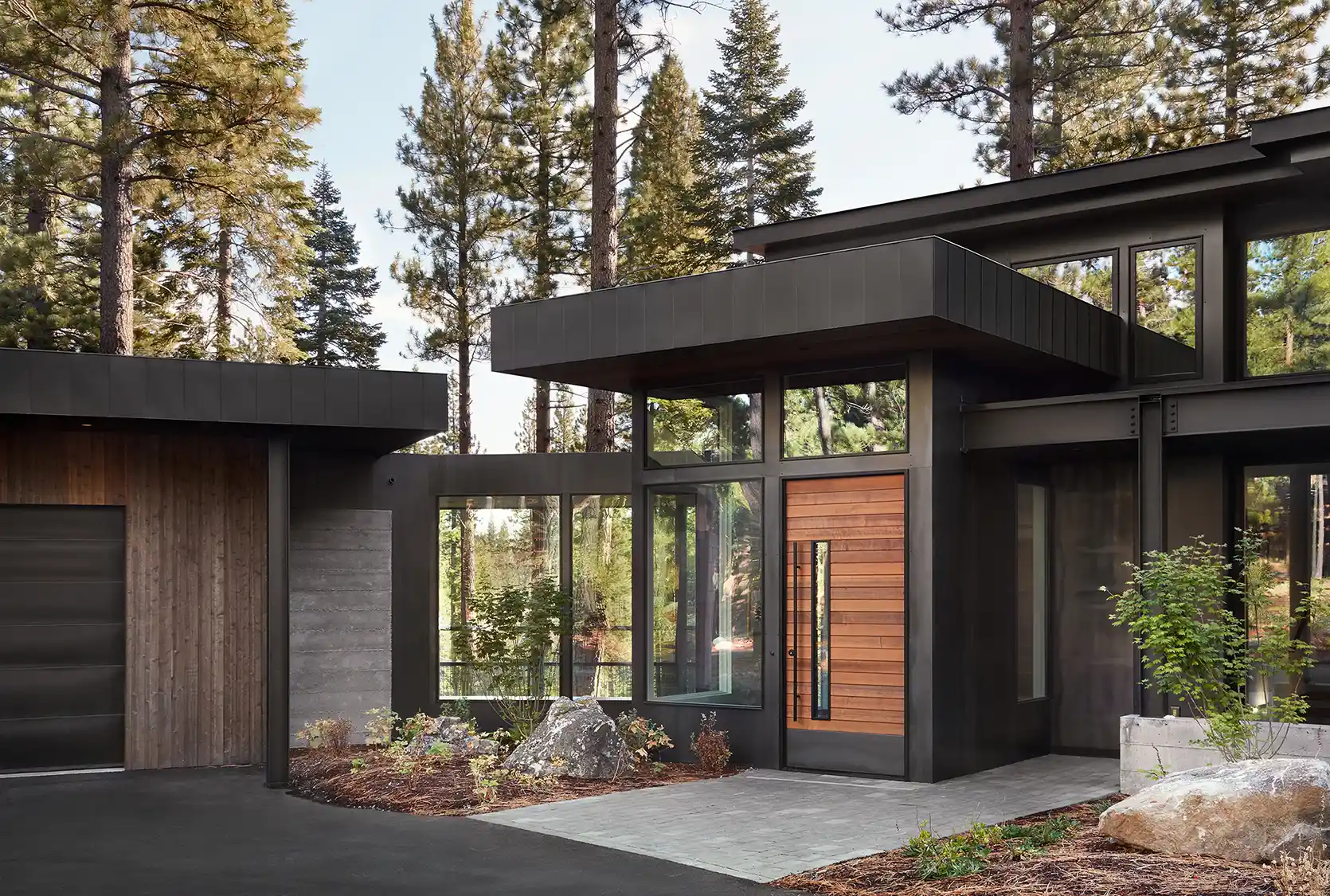 Modern house with wood and concrete exterior surrounded by tall pine trees at dusk.