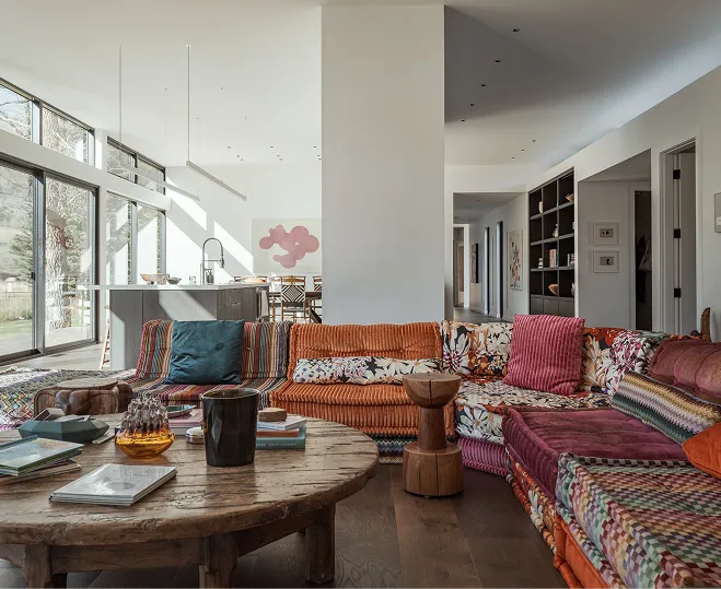 Bright living room with a colorful patchwork sectional sofa, wooden coffee table, and large windows letting in natural light.