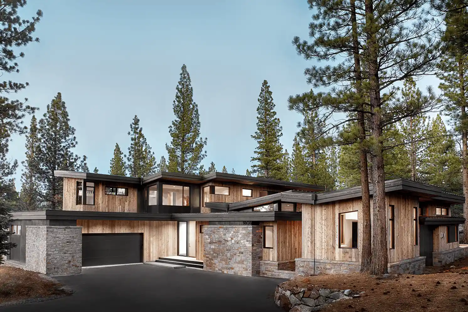 Modern two-story house with wooden and stone exterior, illuminated warm interior lights, surrounded by pine trees at dusk.