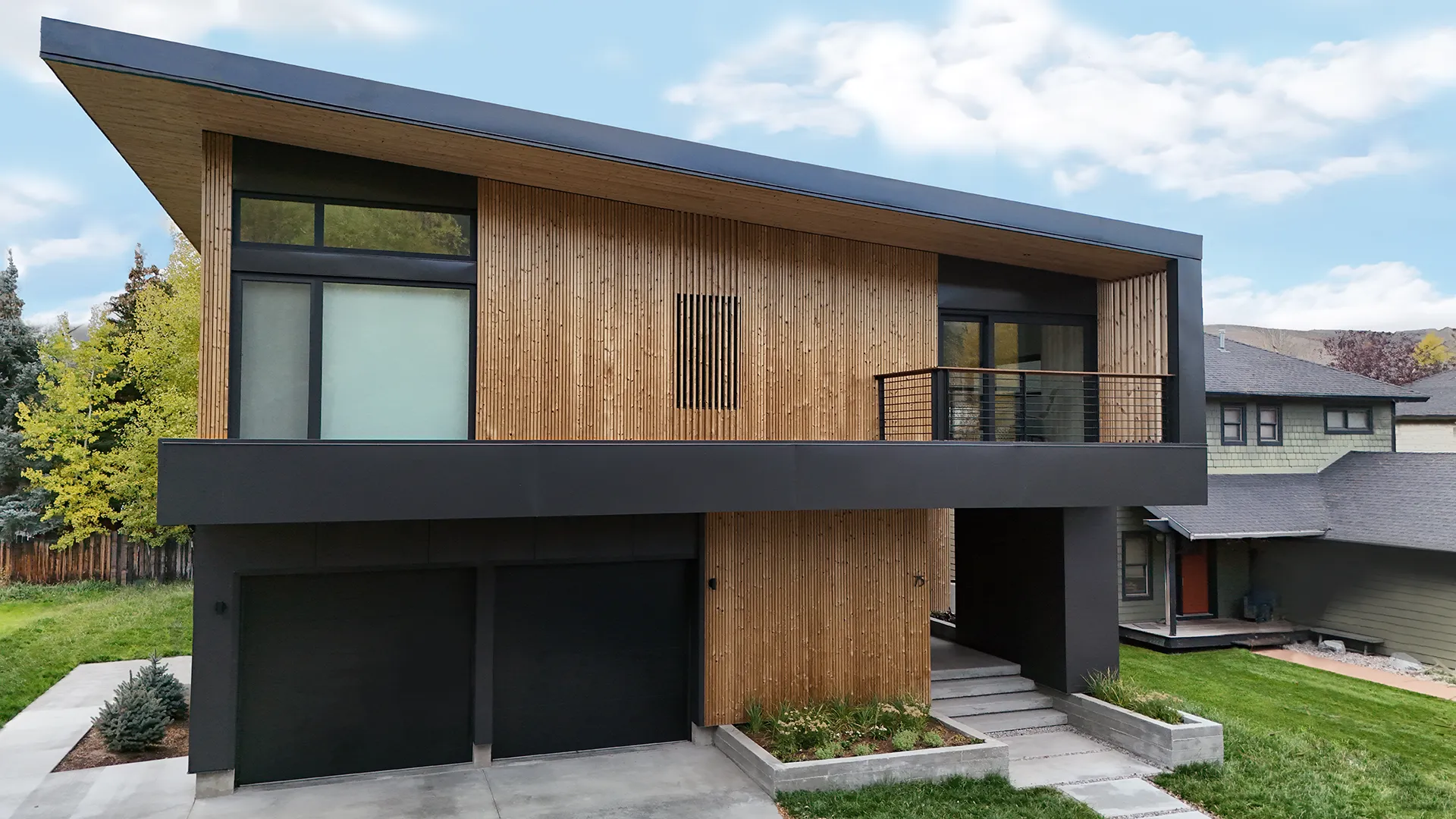 Modern two-story house with wood paneling and large windows under a slanted roof.