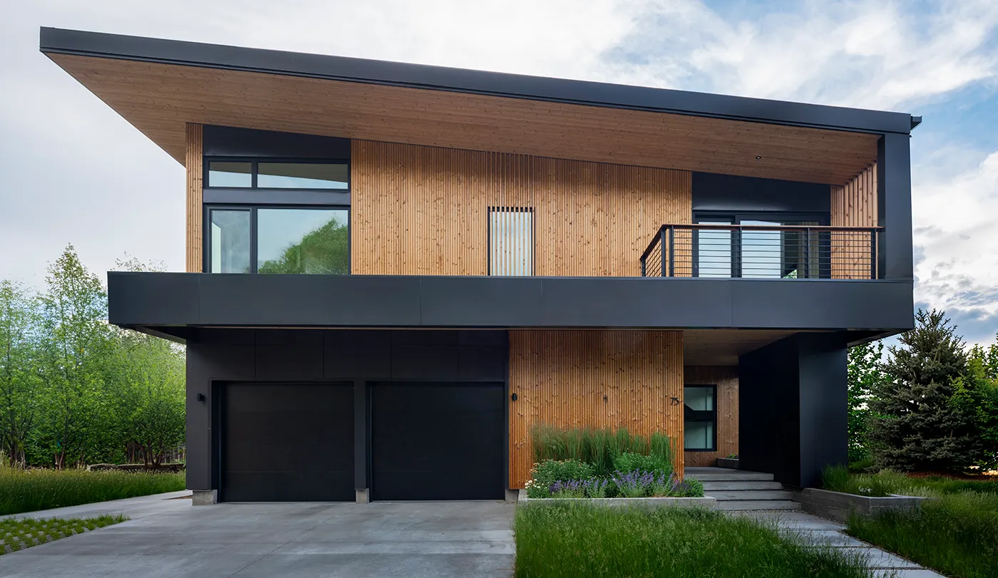 Modern two-story house with black and wood exterior, large windows, balcony, and attached garage.