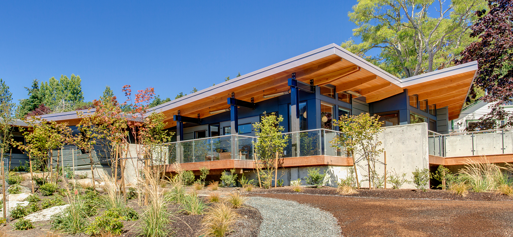 Modern house with upward sloping roof surrounded by landscaping and blue sky.