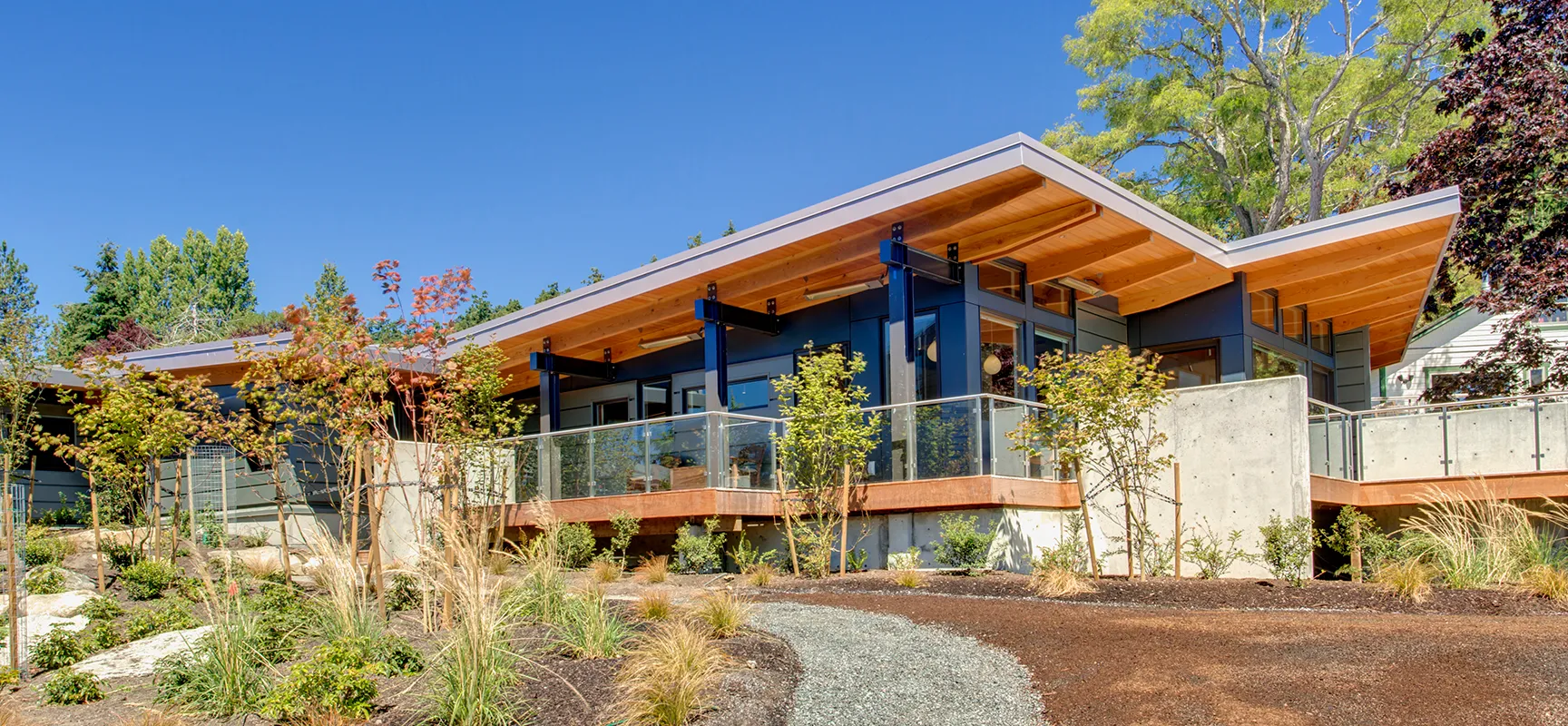 Modern house with upward sloping roof surrounded by landscaping and blue sky.