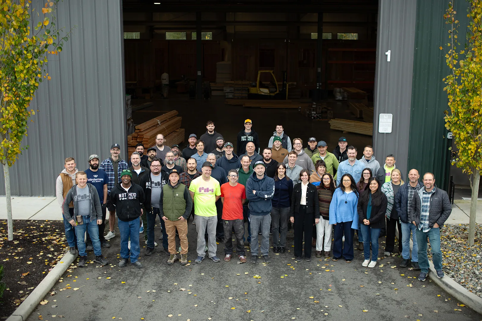 Large group of workers standing outside a factory entrance with wood materials visible inside.