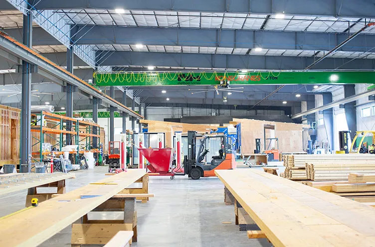 Interior of a large factory with wooden panels, forklifts, and equipment under a high metal ceiling.