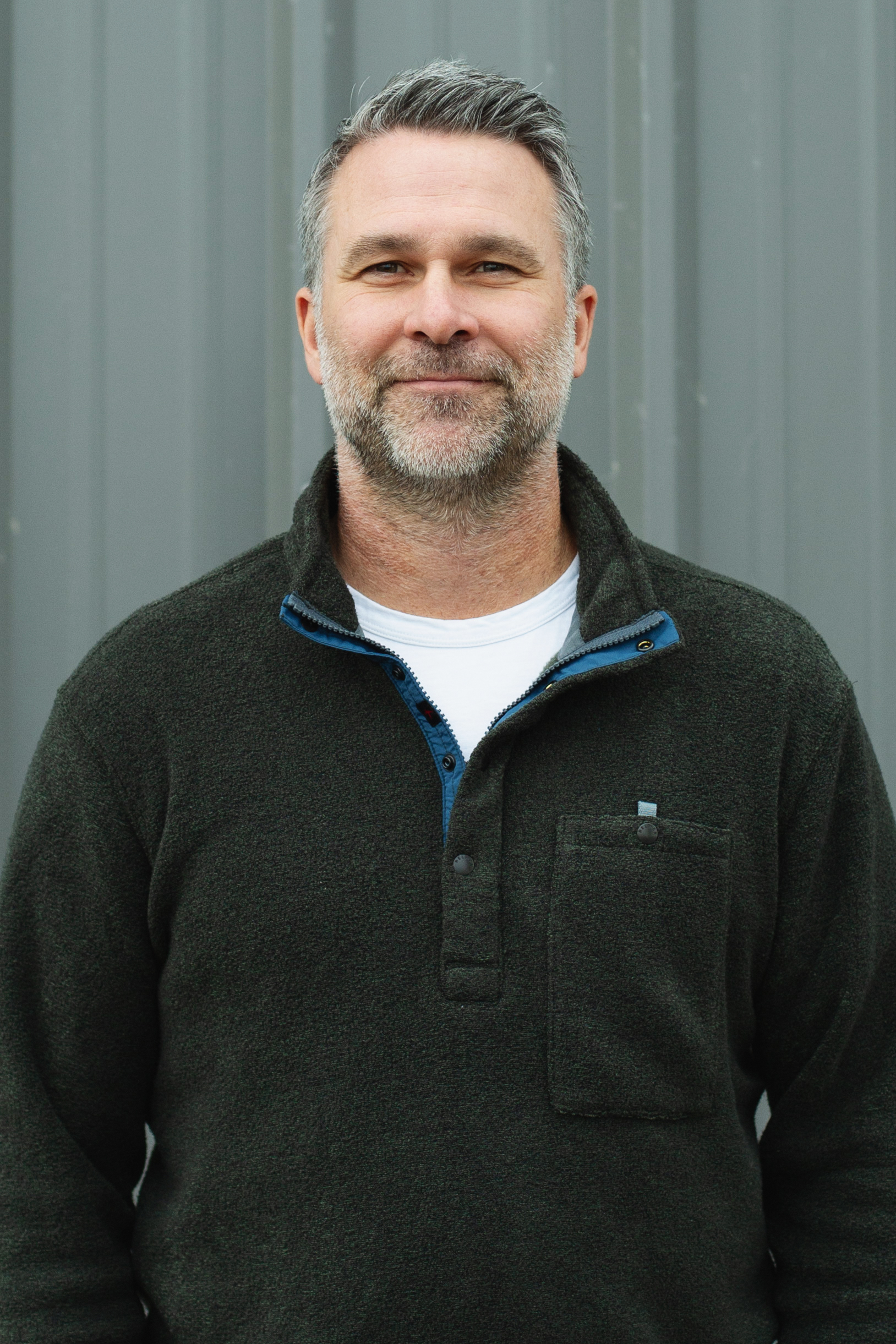 Smiling man with beard wearing a dark fleece pullover over a white shirt.