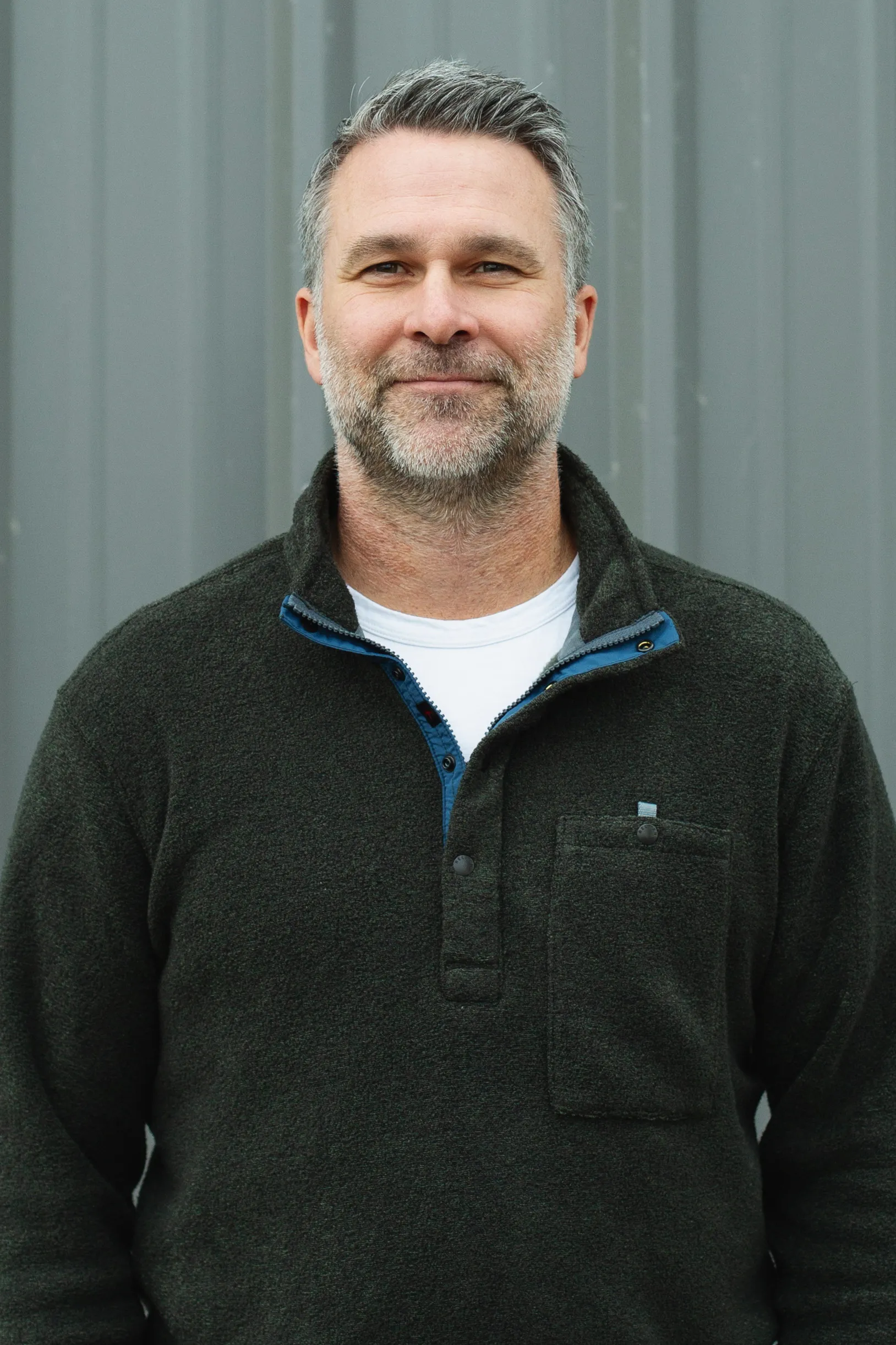Smiling man with beard wearing a dark fleece pullover over a white shirt.