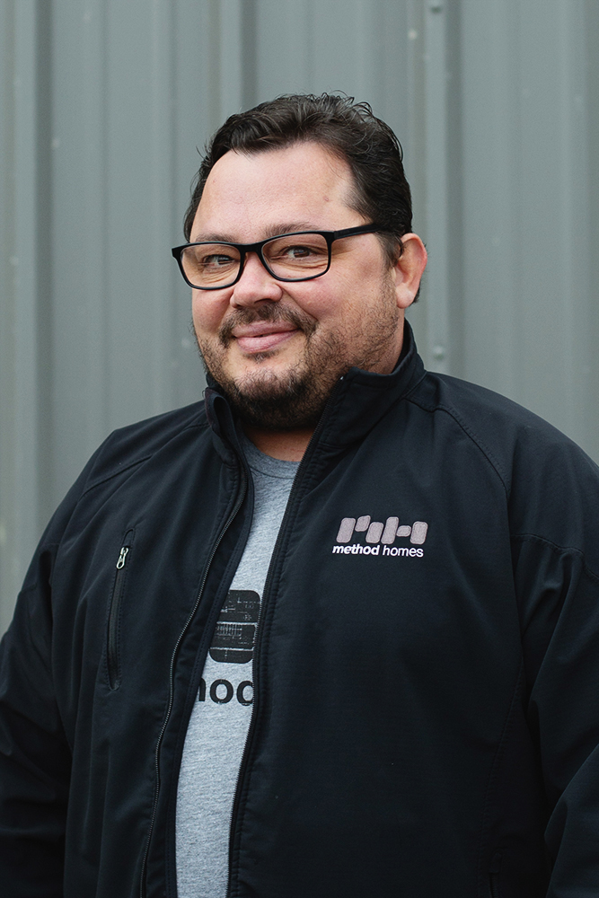 Man wearing glasses and a black jacket with Method Homes logo standing in front of a gray metal wall.