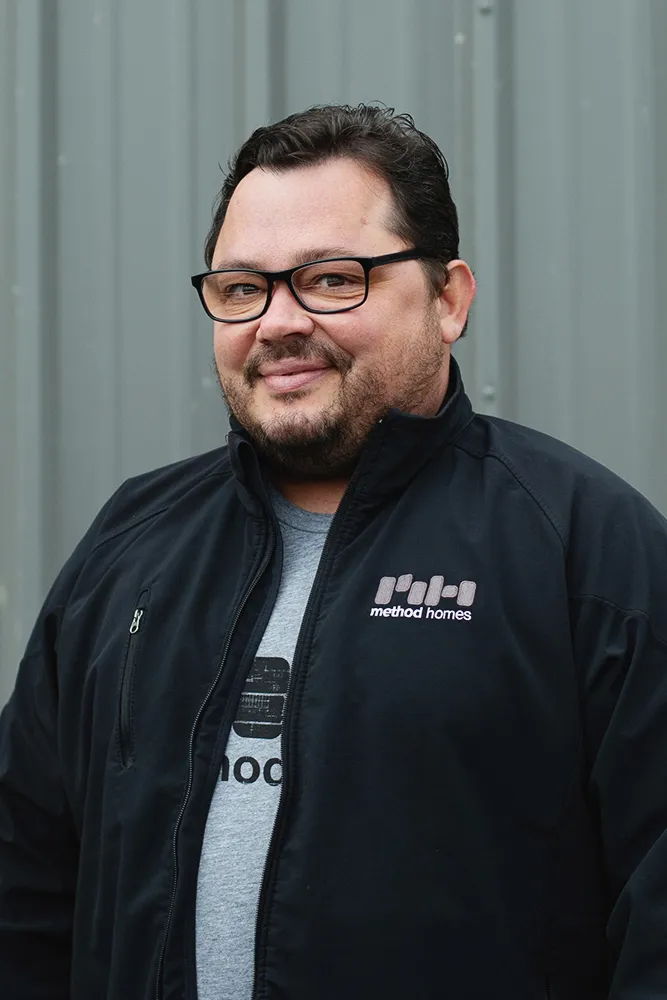 Man wearing glasses and a black jacket with Method Homes logo standing in front of a gray metal wall.