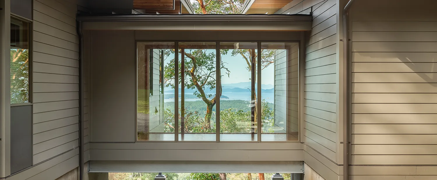Glass bridge connecting two beige buildings with a tree and distant mountains visible through the glass.