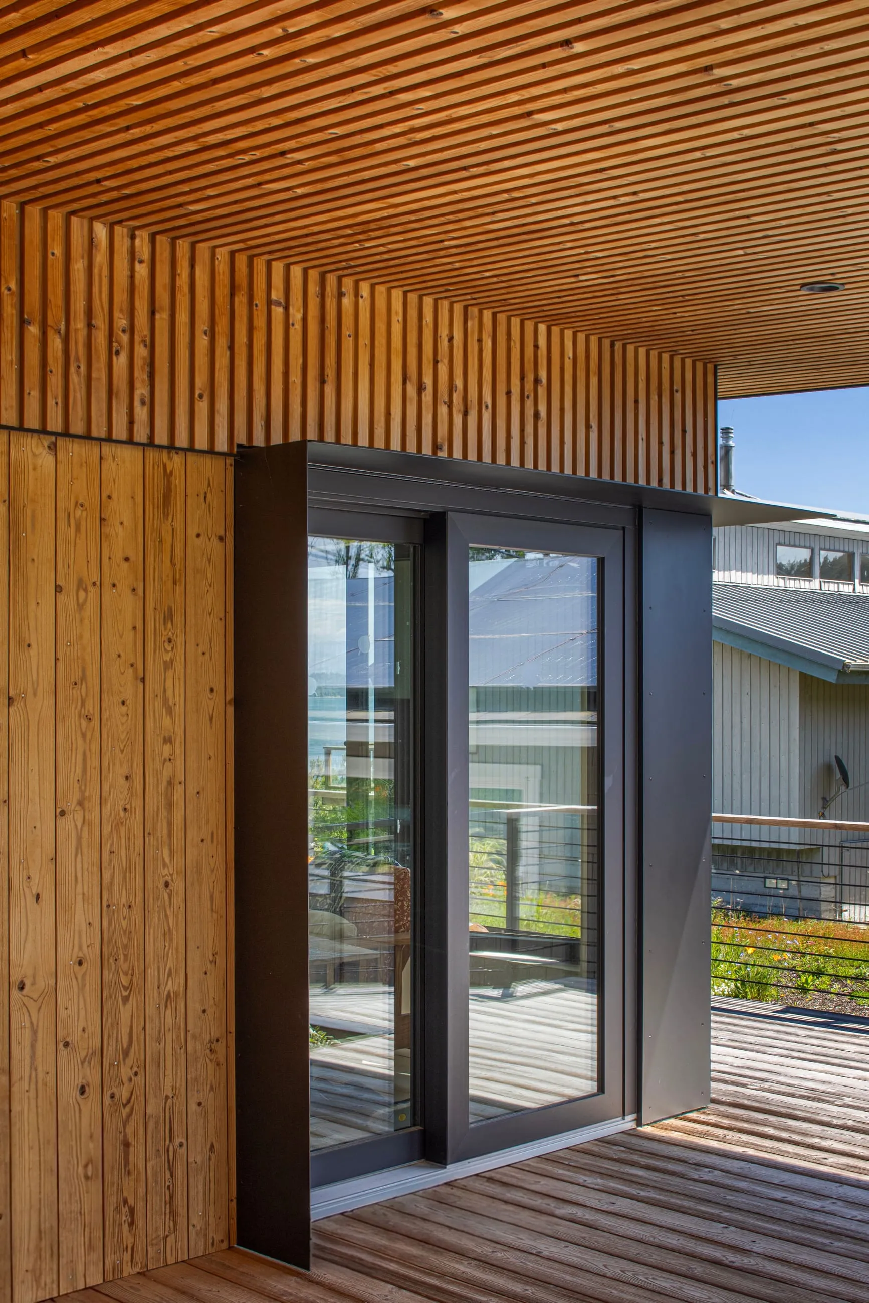 Modern wooden terrace with slatted privacy panels, black metal railings, and glass doors under clear blue sky.