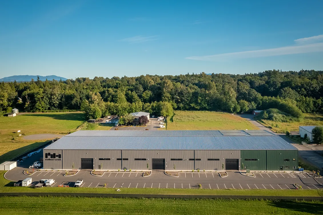 Panoramic view of Method Packaging large warehouse with solar panels on the roof surrounded by fields and trees.
