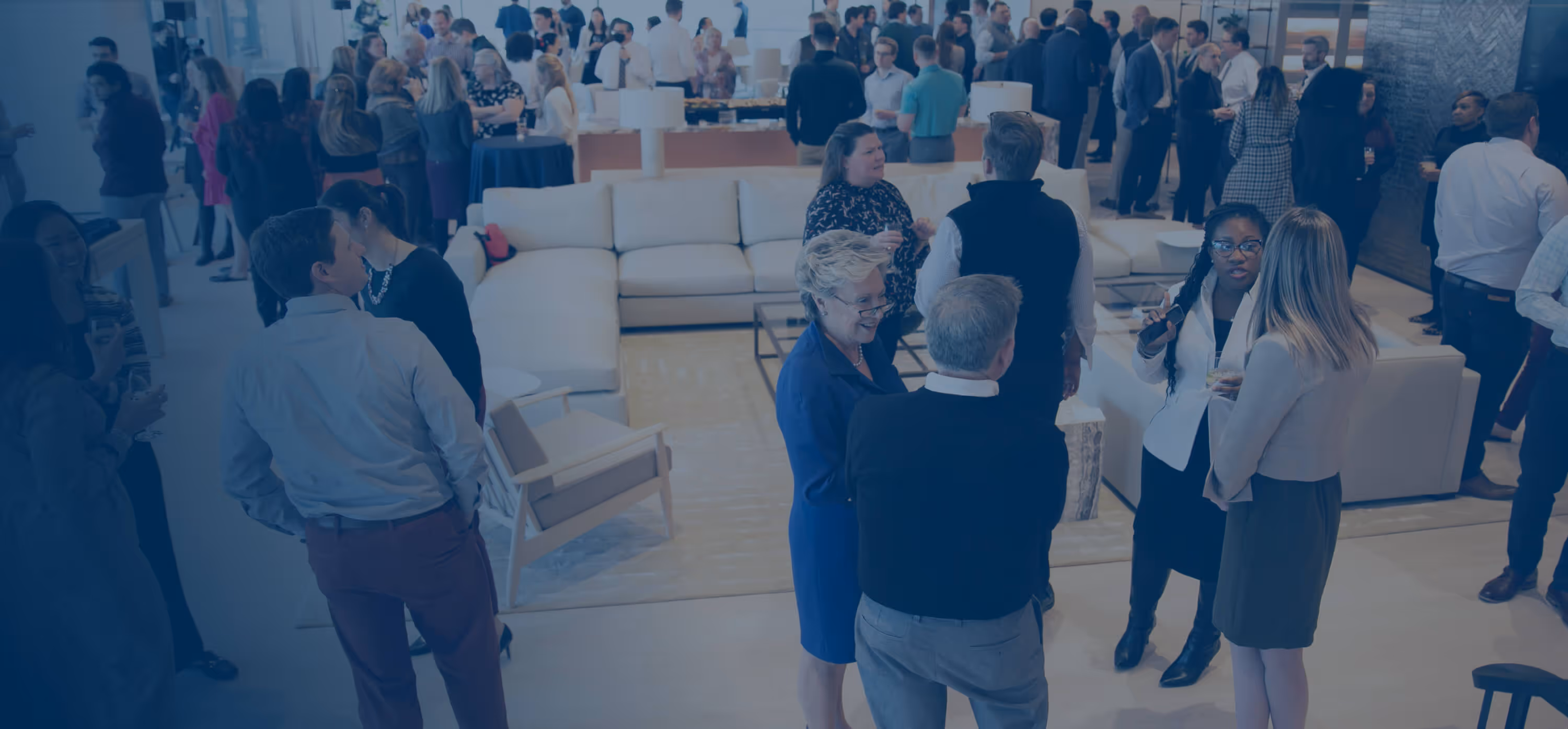 A group of people standing around a room filled with furniture.
