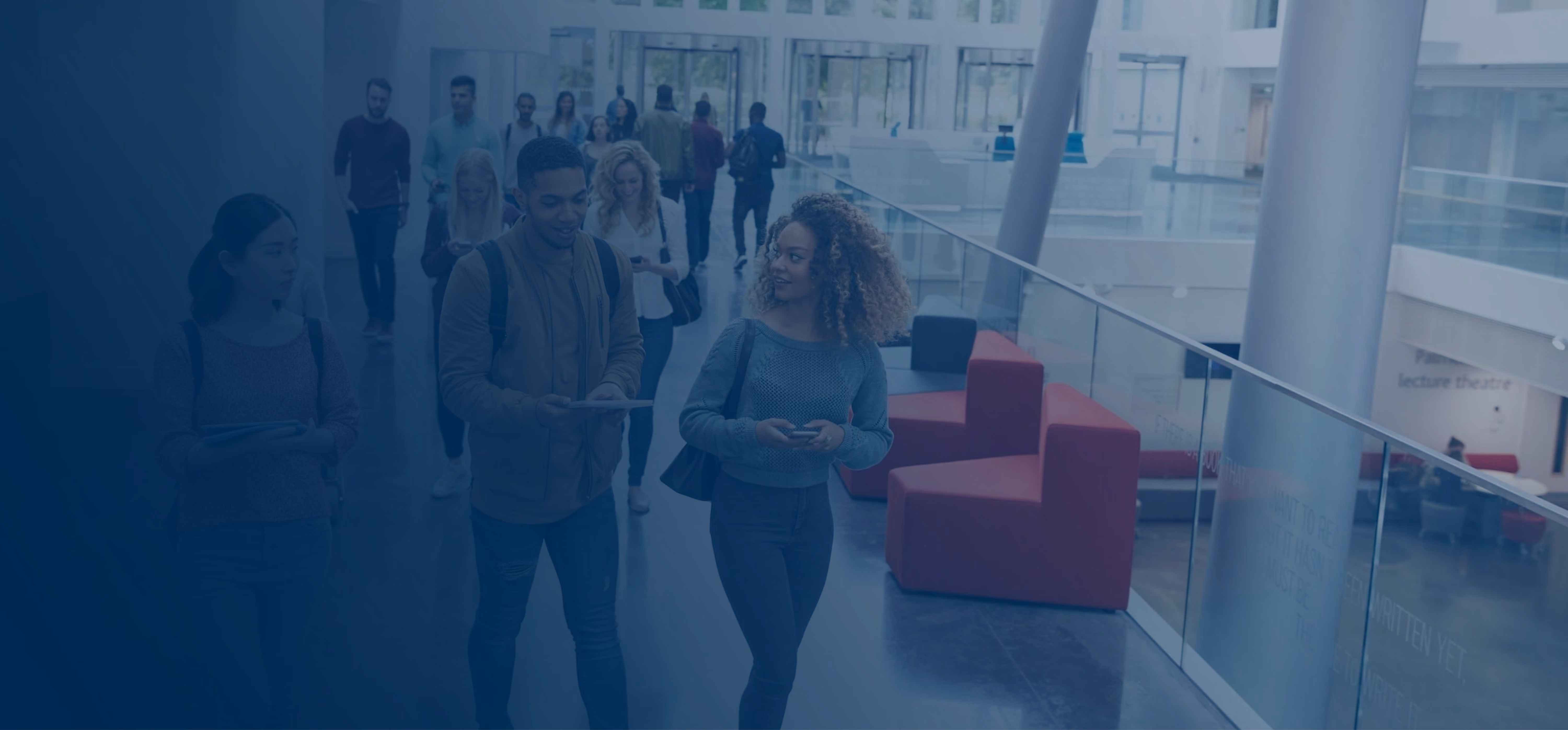 Young adults walking and talking in a modern, bright university or office building hallway.