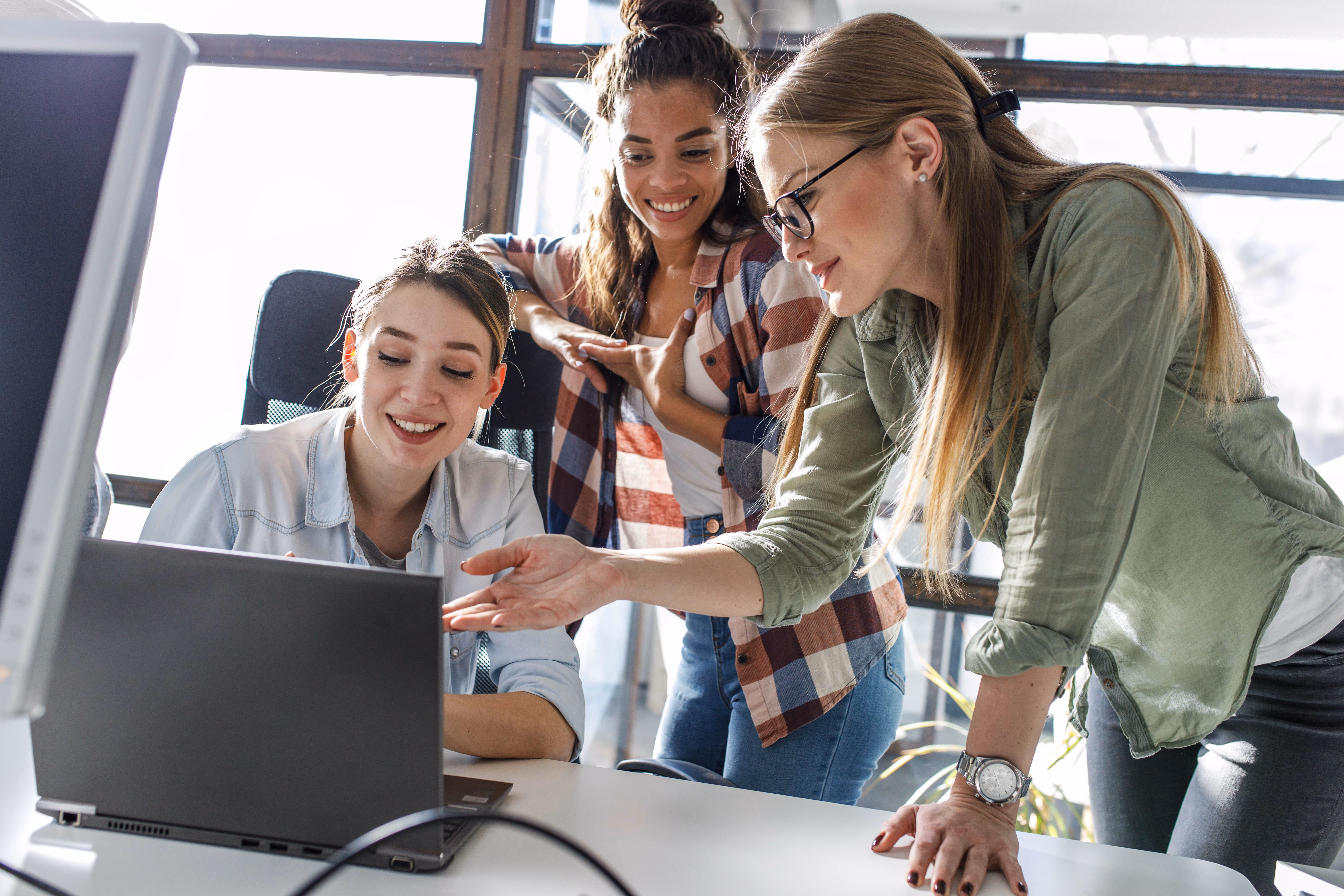 A group of women standing around a laptop computer.