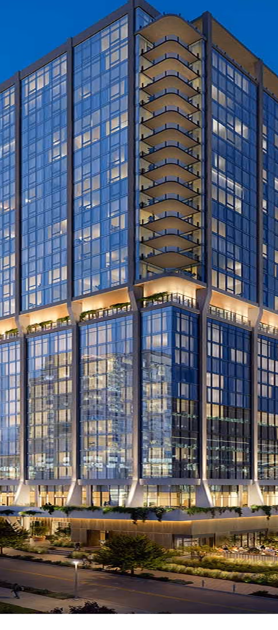 Modern high-rise building with glass facade and balconies illuminated at dusk.