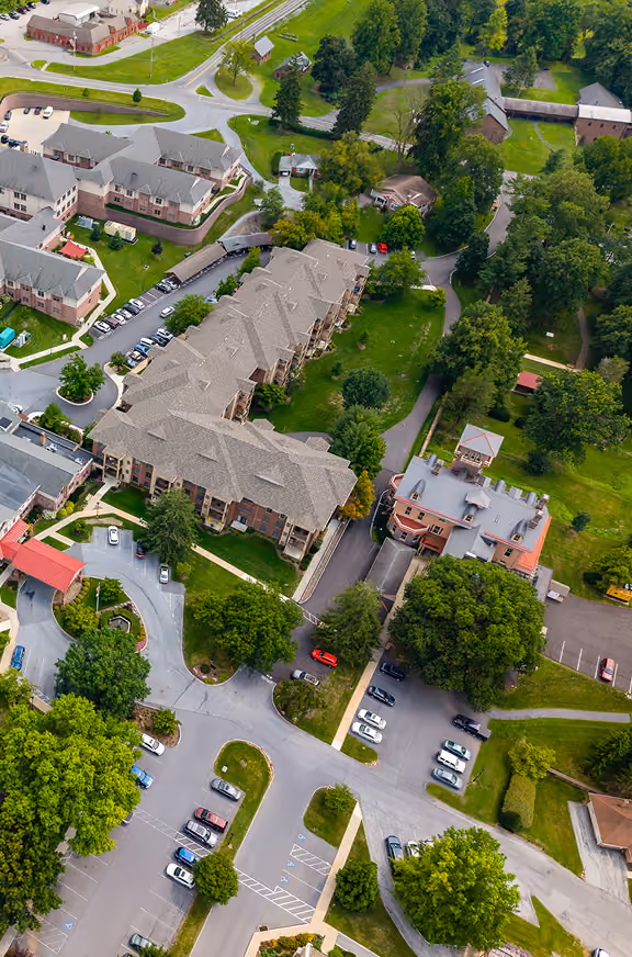 Aerial view of an Owned & Leasehold Portfolio seniors housing campus with brick buildings, tree-lined lawns and parking