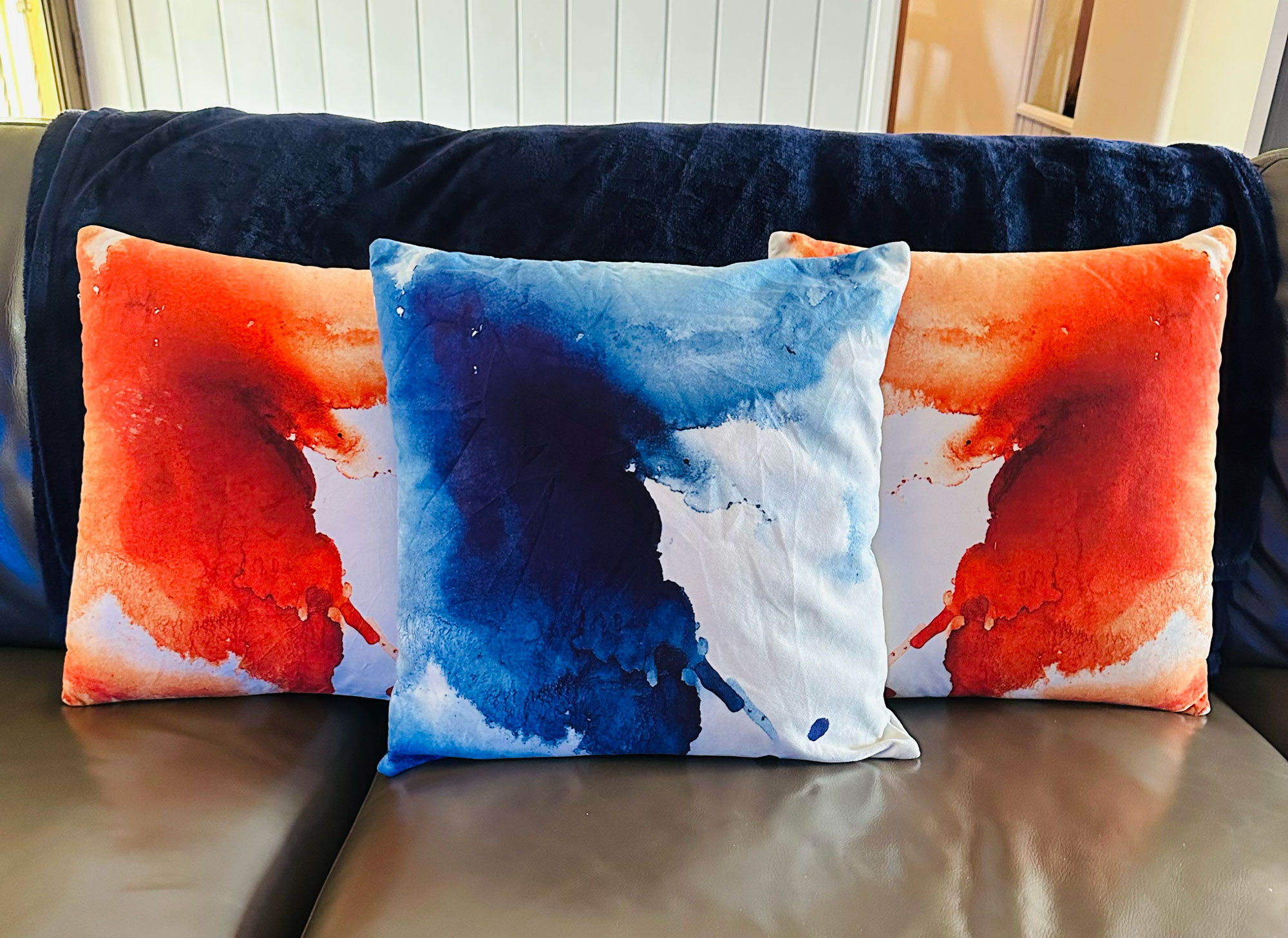 Three cushions custom printed with a splatter design in orange and dark blue