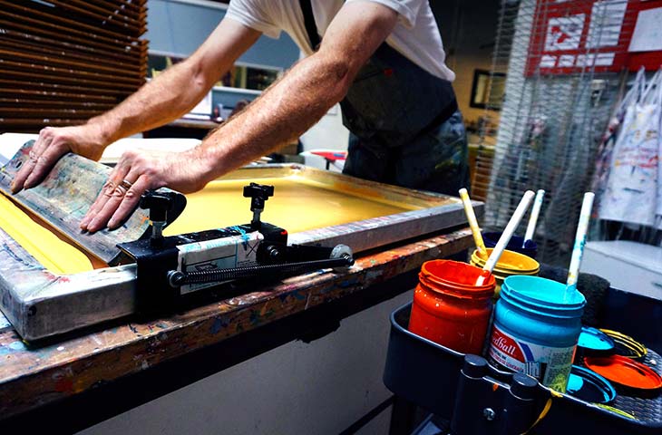 Man pulling a squeegy over a screen to screen print it