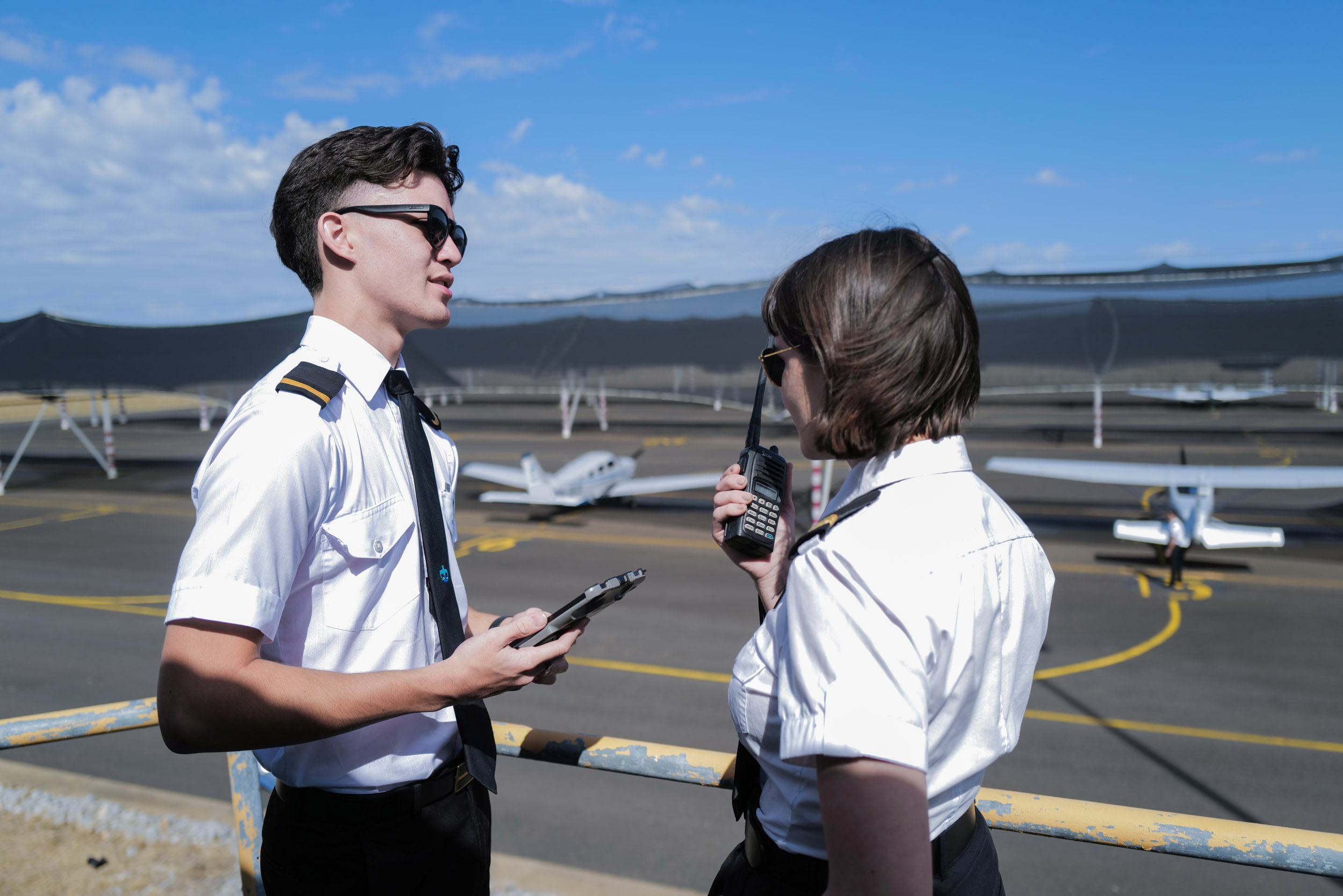 Two student pilots on a balcony looking at the runway at SFC Pilot Academy Tamworth. One is talking on a radio.