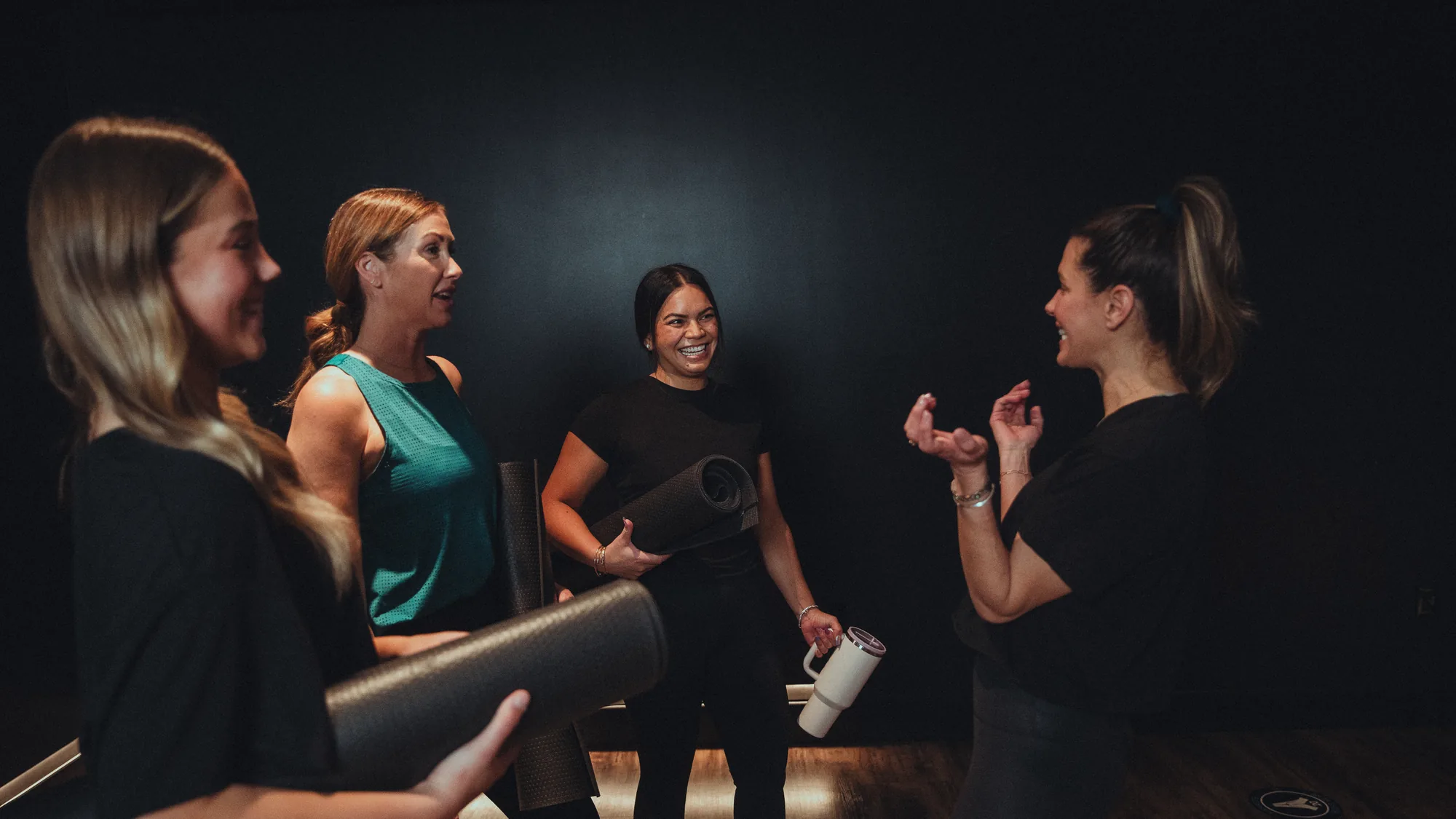 An instructor and three members chatting and laughing with their mats after class at a boutique studio