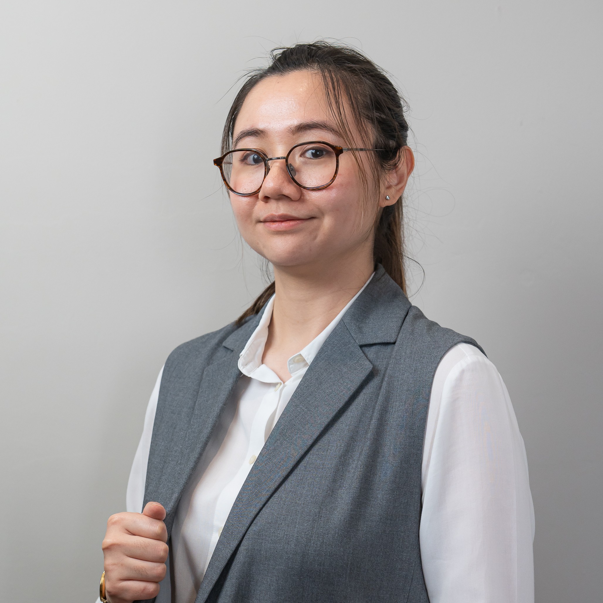 Man wearing glasses and a suit with a 'GUIDE' lanyard, standing indoors with hands clasped.