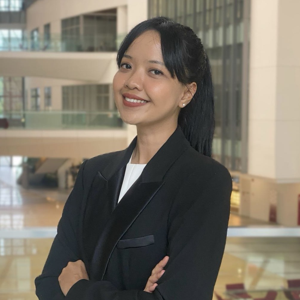 Man wearing glasses and a suit with a 'GUIDE' lanyard, standing indoors with hands clasped.