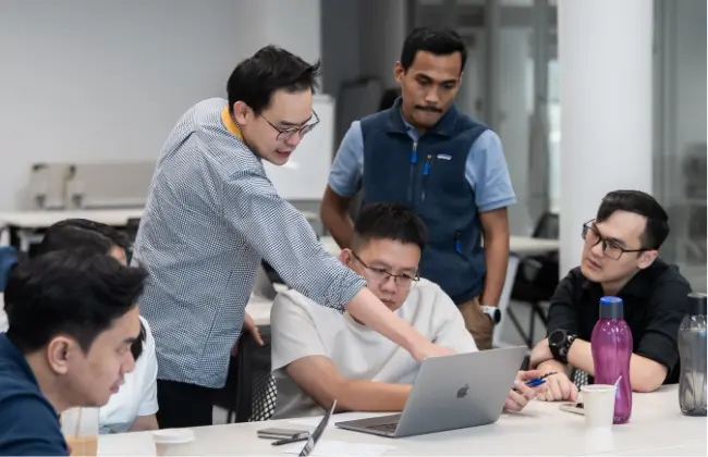 Five men collaborating around a laptop in a modern office setting.