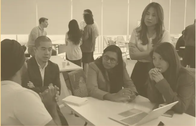 A group of five people engaged in a discussion around a table with a laptop and notebook.