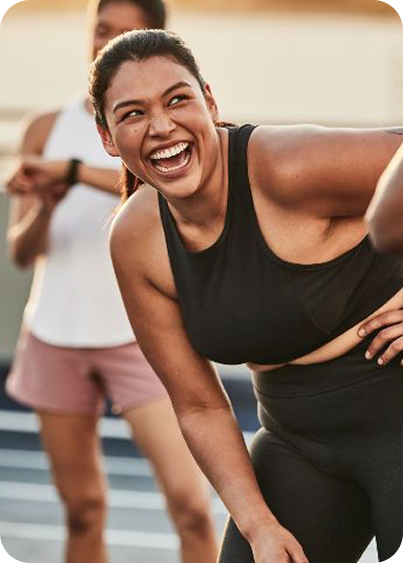 Smiling woman in black workout clothes leaning forward during outdoor exercise session.