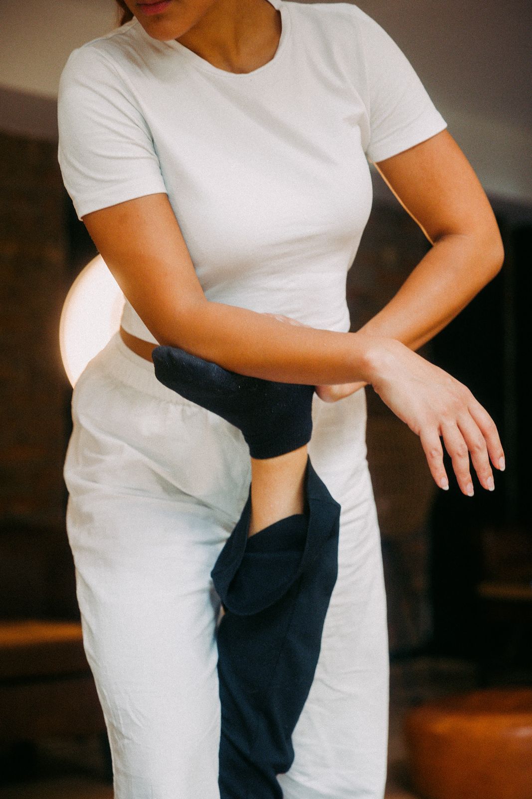 Person wearing a white shirt and pants balances a foot raised behind with a black sock.