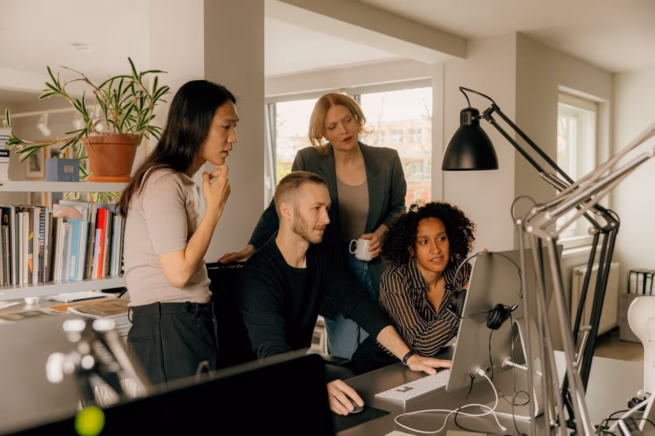 Four colleagues gathered around a screen in discussion — reflecting the cross-functional problem-solving that follows when be