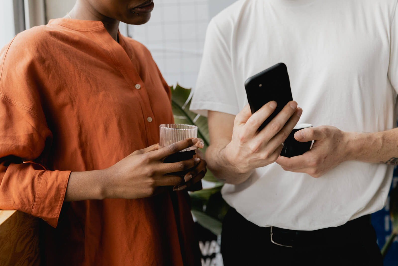 Two colleagues chatting over coffee, one holding a phone, in a casual moment that reflects the informal conversations where b