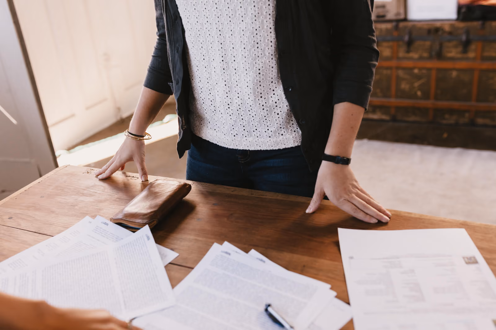 A person standing at a wooden table covered in documents and reports, hands resting on the surface, evoking a budget review o