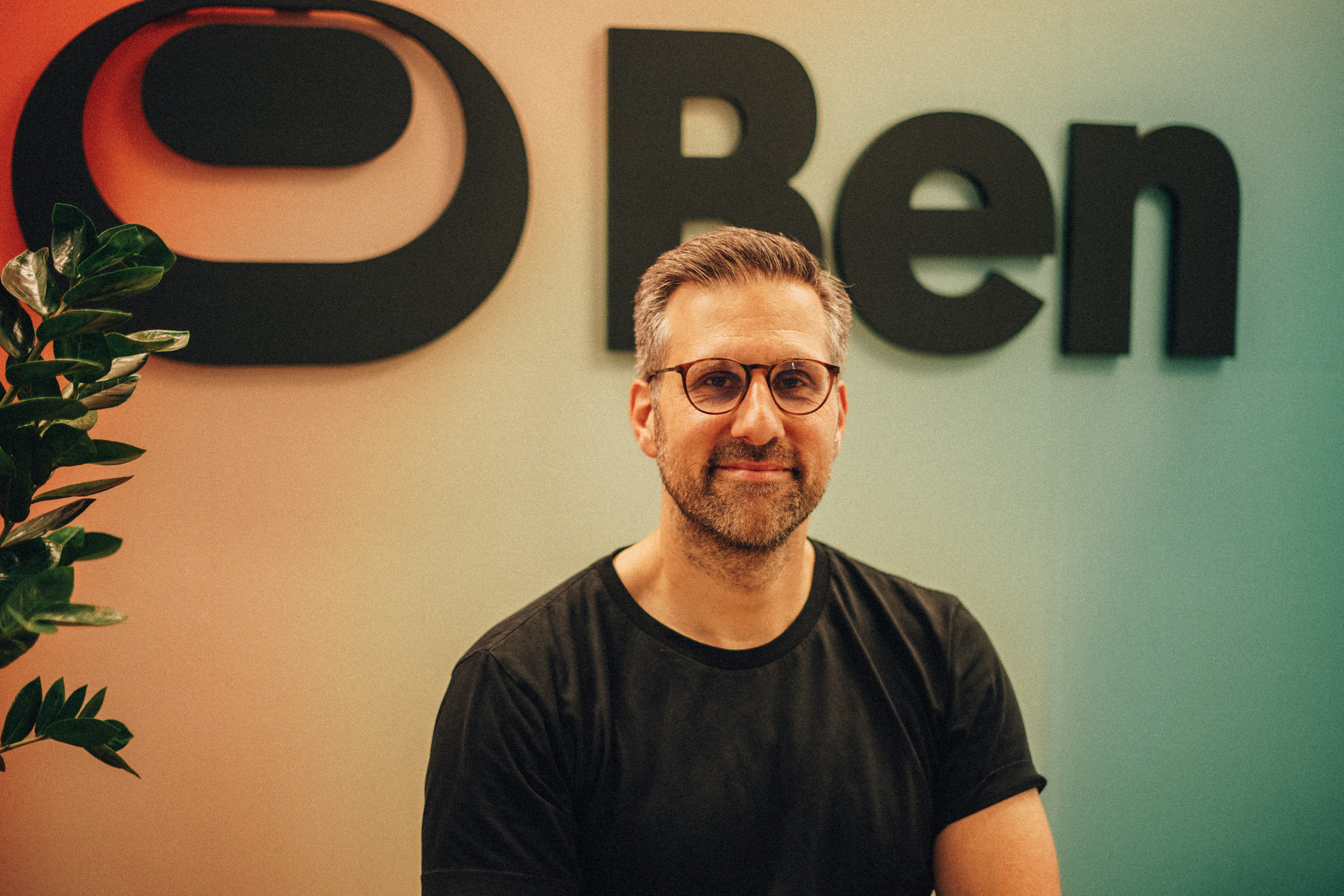 Seb Fallert, CEO of Ben, smiling in front of the Ben logo on the company's office wall.