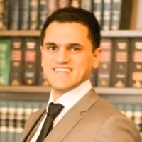 Young man in a suit and tie smiling with bookshelves in the background.
