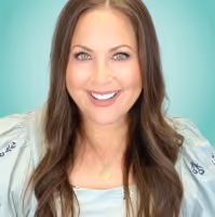 Smiling woman with long brown hair wearing a light blue top and gold necklace on teal background.