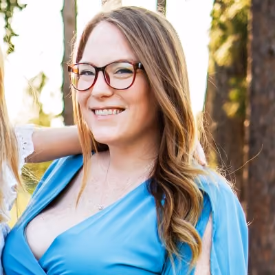 Smiling woman with long light brown hair and glasses wearing a blue dress outdoors.