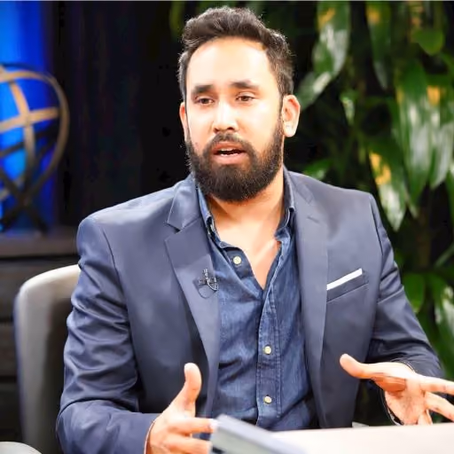 Bearded man in blue blazer discussing while sitting with plants and a globe in the background.