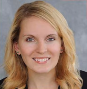 Smiling woman with long blonde hair and light eyes against a gray background.