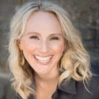 Smiling woman with curly blonde hair wearing a black top and gold earrings.