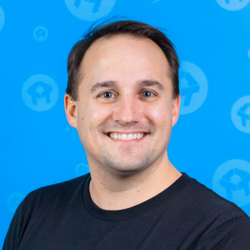 Smiling man with short dark hair wearing a black shirt against a blue background with white logos.