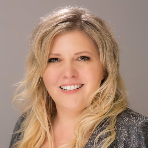 Smiling woman with long wavy blonde hair wearing a textured gray blazer against a neutral background.