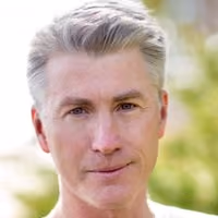 Middle-aged man with gray hair and blue eyes looking at the camera outdoors.
