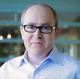 Middle-aged man with glasses wearing a blue checkered shirt in an office setting.